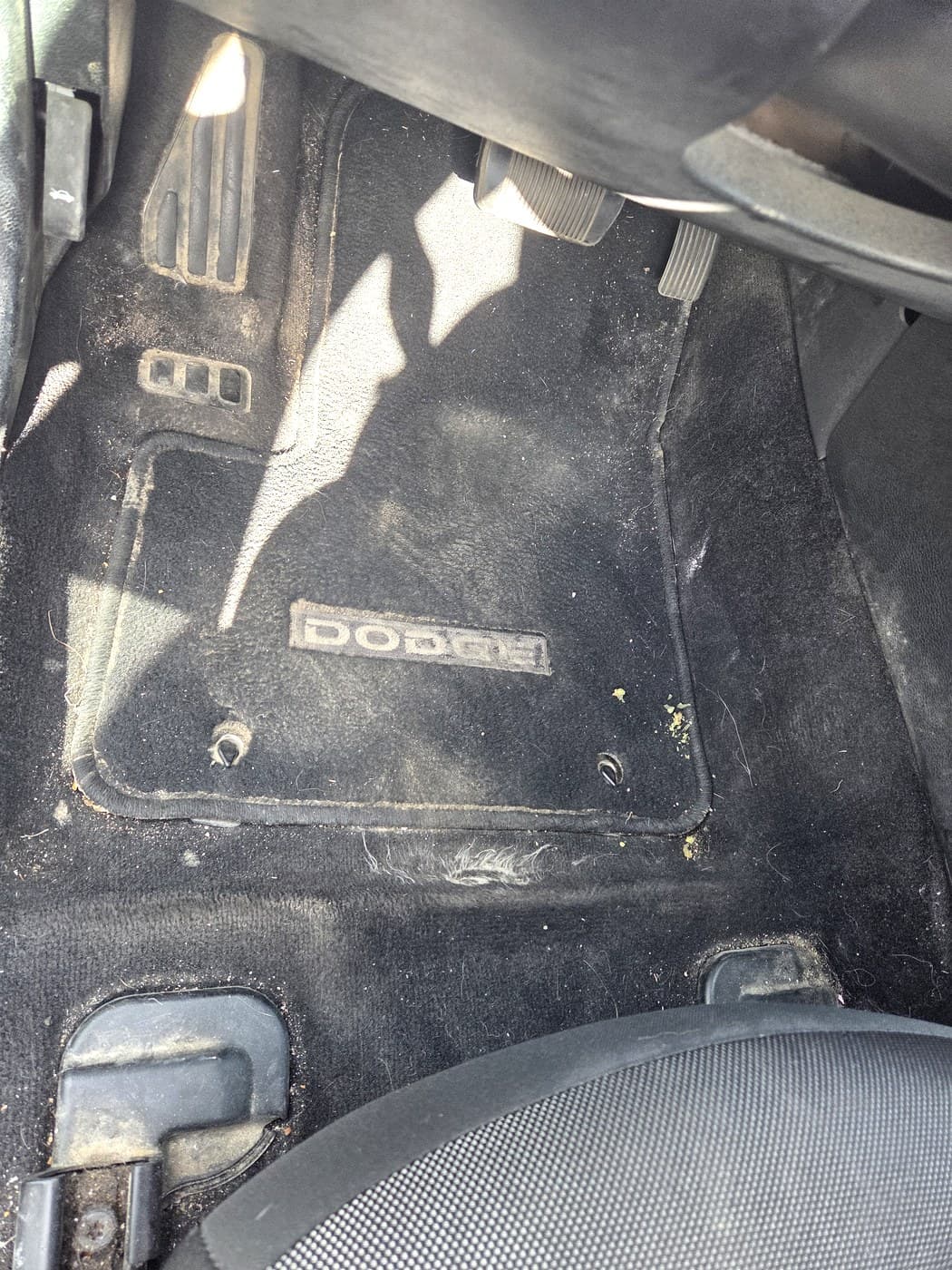 Driver side floor before cleanup with the floor mat installed and debris visible.