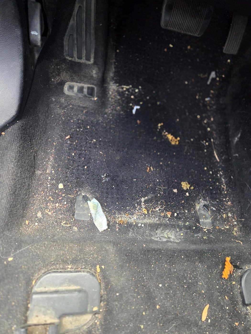 Driver side floor before cleanup with the floor mat removed and loose debris visible.