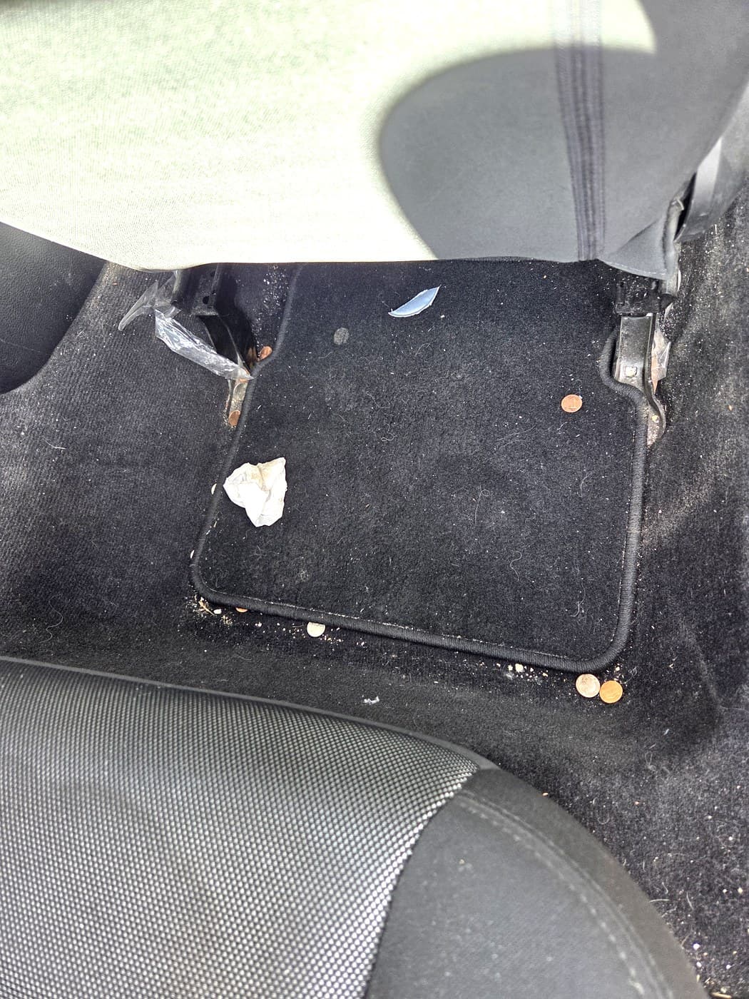 Rear passenger floor before cleanup with snack crumbs and debris on the mat.